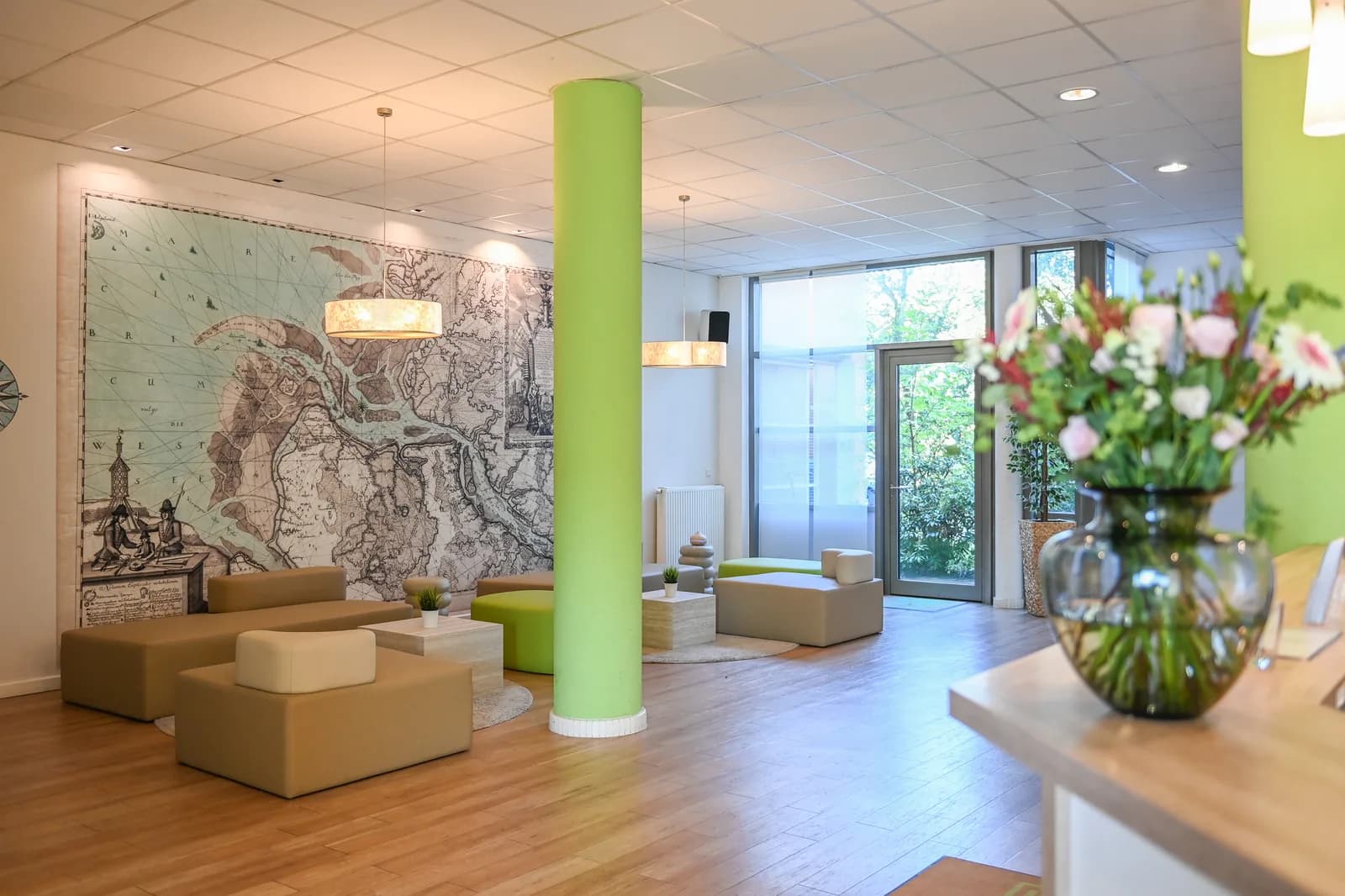 Lobby van Hotel NordRaum met zitgroep, groene zuil en bloemboeket bij de receptie