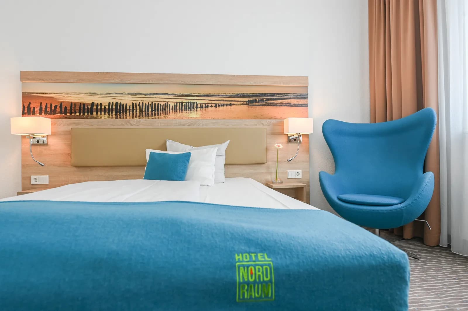 Tweepersoonsbed met strandpanorama op het hoofdbord en blauwe fauteuil