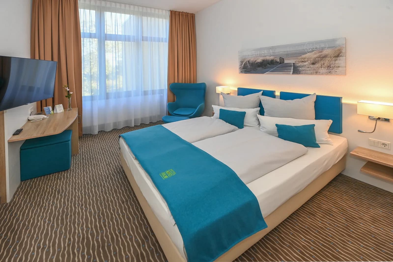 Doppelzimmer mit Sessel am Fenster und blauem Kopfteil