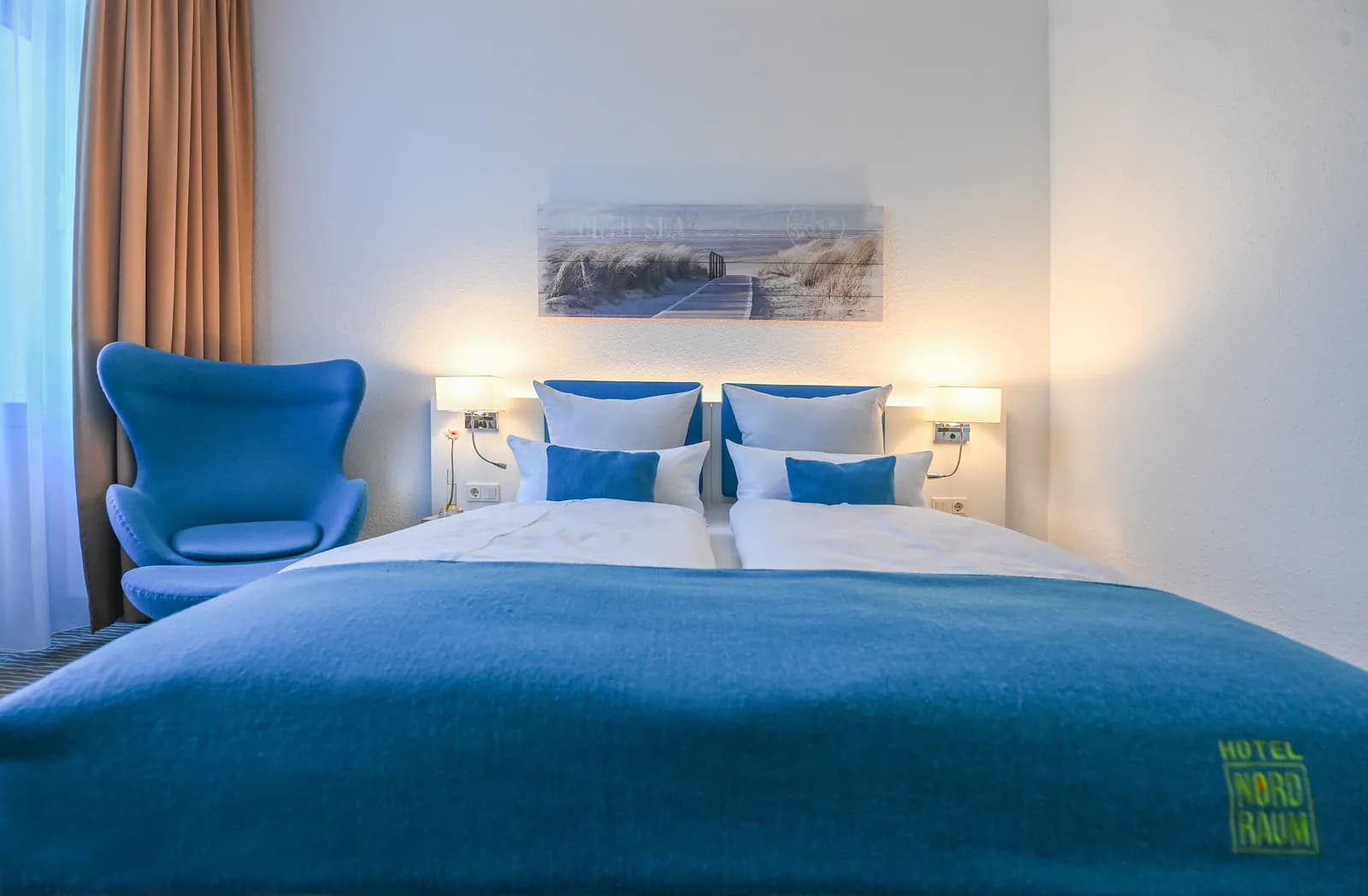 Room with two beds, blue headboards and an armchair